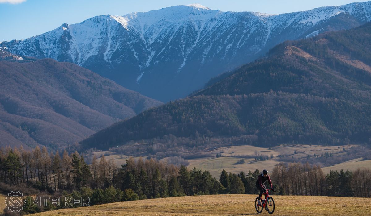 cyklista na bicykli, v pozadí zasnežené hory